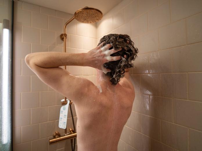 Mand der tager brusebad. Han slukker for vandhanen når han tager shampoo i håret. 